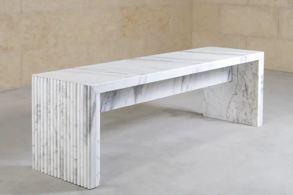 Modern white marble bench with fluted side panel design on concrete floor and beige wall
