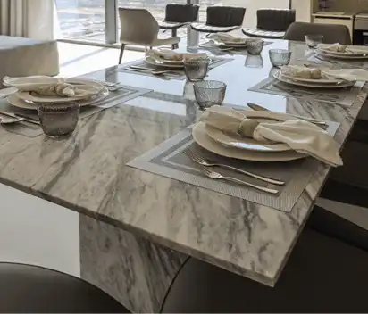 Modern dining table with gray marble surface set with plates, folded napkins, cutlery, and drinking glasses