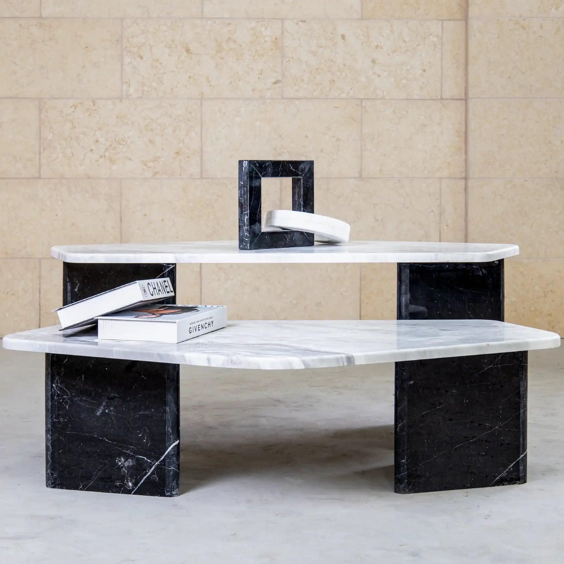 Modern coffee table with marble top and black marble legs against a beige tiled wall.
