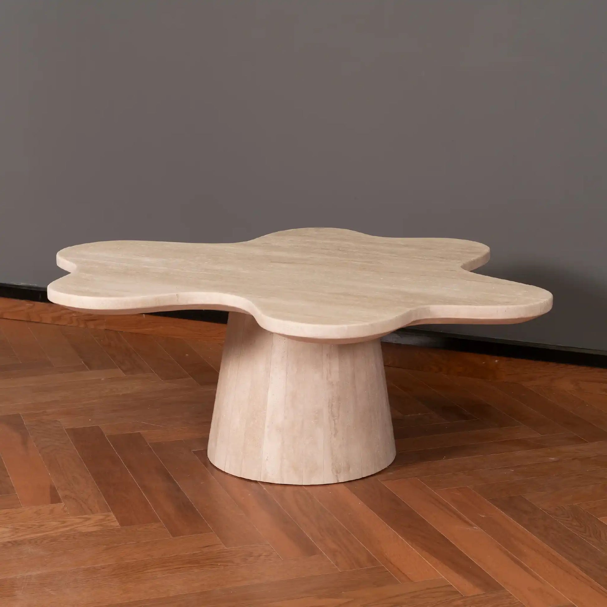 Petalo Travertine coffee table with a unique design on a wooden floor and gray wall background.