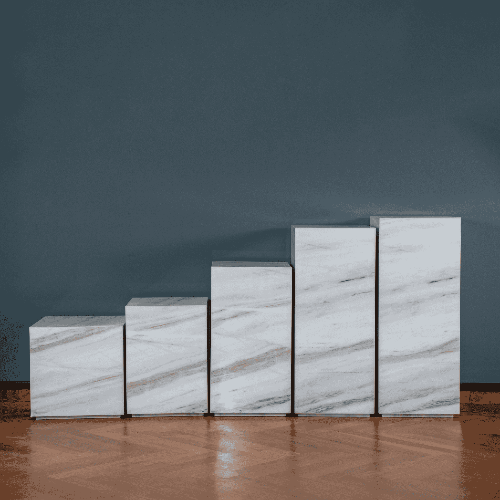 Set of marble plinthes against a dark blue wall on a wooden flooring